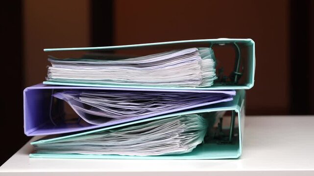 Stack of colorful ring binders overflowing with various business documents, financial records, and archived paperwork, representing office organization, administration, and legal compliance