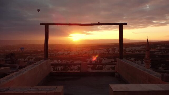 Sunset rooftop terrace is overlooking cappadocia city at sunset. Minaret silhouette against warm sky at golden light spilling over stone benches. Peaceful evening atmosphere ideal for travel marketing