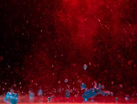Water droplets and spray surround a person standing beneath red stage lights