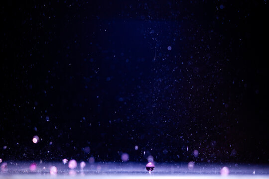 Water droplets fall onto a surface under blue and purple light