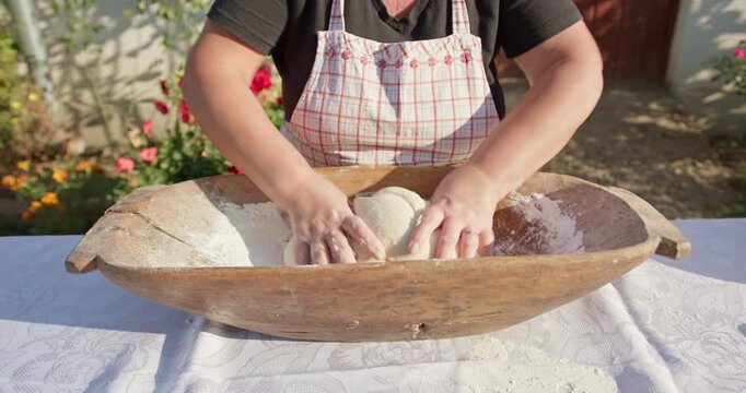 Woman kneading dough in an antique wooden trough outdoors