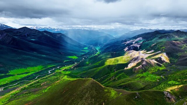 Dramatic high-angle view of lush mountain valleys and winding riverbed under stormy clouds in Sichuan, capturing majestic alpine terrain.