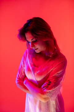 Warm magenta accents on textured fabric background. Subtle glamorous representation featuring thoughtful model under glowing neon illumination with textured clothing