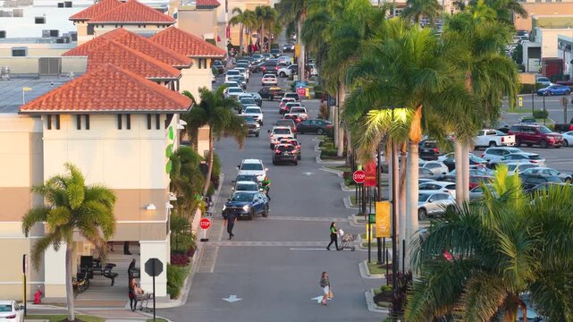 Large retail complex with pedestrians entering stores, crossing traffic lanes and cars driving slowly. Active consumer behavior concept.