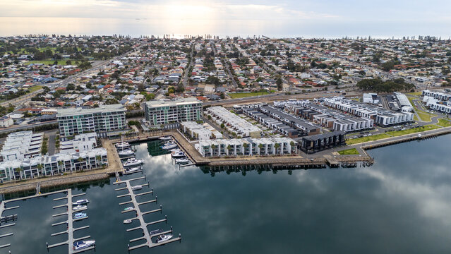 Aerial drone view over the New Port waterfront development at Port Adelaide, South Australia, with rows of townhouses and apartment buildings lining the marina, boats moored at floating pontoon 