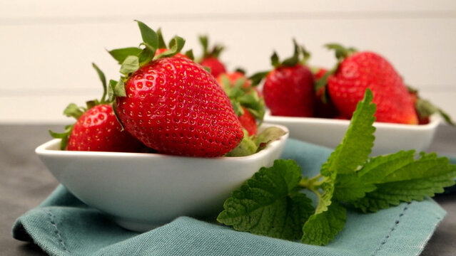 Fresh strawberries in white bowls with green mint leaves on a blue cloth