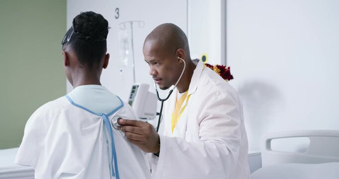 African doctor and patient at bedside in white coat placing steth on blue-tied gown checking lungs