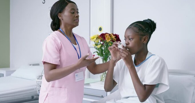 Adult nurse offering inhaler and guiding youth patient inhaling on hospital bed for device training