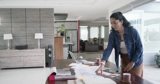 Indian woman at home touching laptop at large table, sorting plans, swatches for layout, copy space