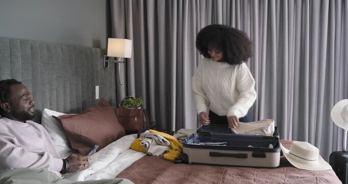 African American couple, woman unfolding garment and packing suitcase in hotel bedroom for trip