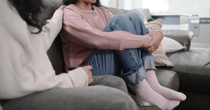 Indian female friends, friend reaching, placing hand on shoulder, calming mature woman on couch
