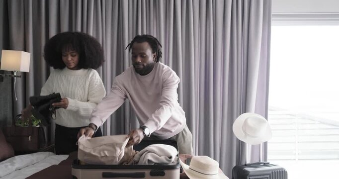 African American couple packing for travel in hotel room, placing yellow jacket and black boots