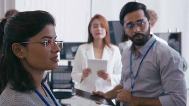 Businesswoman Explaining Ideas to a Male Colleague Holding a Tablet During a Technology Office Discussion with Other Coworkers in the Background