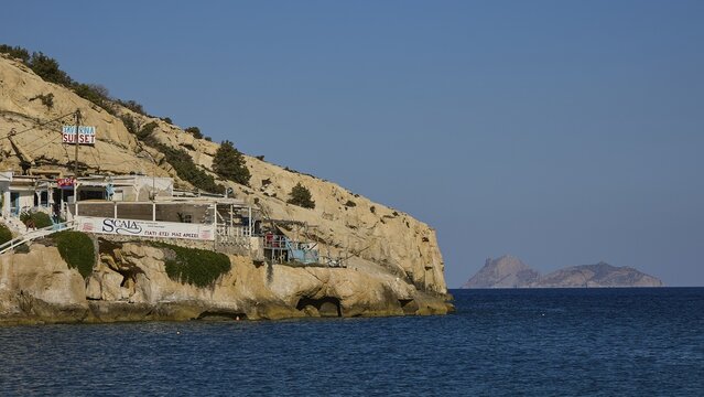 Bars and buildings on a rocky coast with views of the blue sea and distant islands, Matala, South Coast, Crete, Greek Islands, Greece