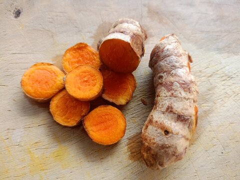 Fresh turmeric root sliced on rustic wooden cutting board