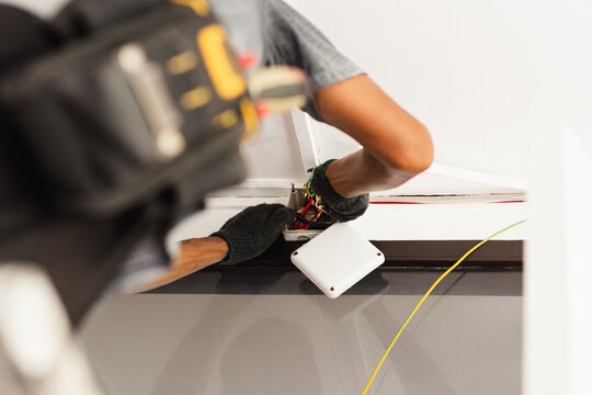 Electrician wearing protective gloves wiring an indoor wall junction box.