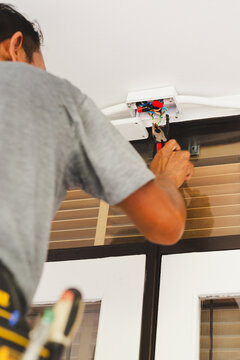 Electrician using pliers to work on electrical wiring inside an open wall mounted junction box.