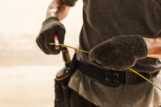 Electrician wearing work gloves using wire pliers to cut a ground cable.