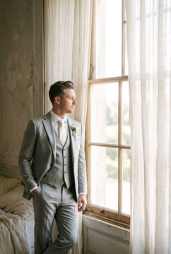 Groom in Light Grey Suit Standing by Window, Wedding Morning Preparation and Anticipation Concept