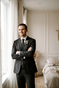 Handsome Groom in Charcoal Suit Standing by Window, Wedding Morning Preparation and Elegance Concept
