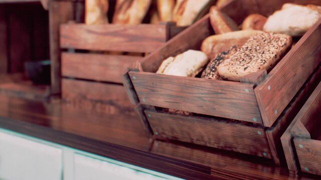 Assorted loaves of fresh bread rest inside rustic wooden crates arranged on a bakery counter, showing various baked goods ready for customers to buy during the day