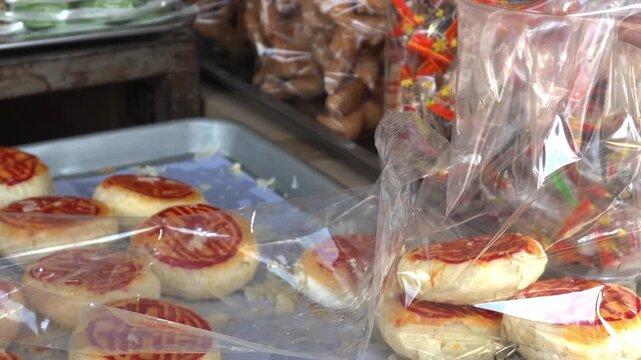 Khmer Vendor Hands Packing Karipap Pastry and Num Pia Cakes in Plastic Bag Battambang
Static tripod medium close-up shot of a Cambodian vendor wearing plastic gloves packing traditional crescent Kari