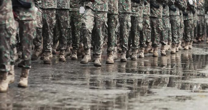 Romanian army soldiers march during a military ceremony on a rainy day.