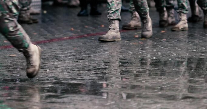 Romanian army soldiers march during a military ceremony on a rainy day.
