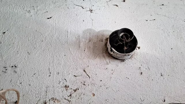 Old electrical socket mounted on a cracked, weathered white plaster wall, showing exposed internal wiring and a worn surface in an aging building, illustrating electrical repair and maintenance