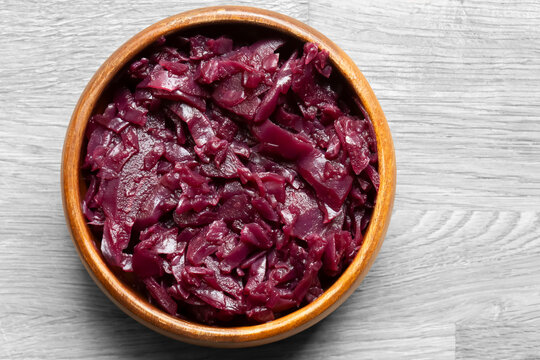 Red cabbage, braised in red wine with apple, in a brown wood bowl background backdrop. On a wooden chopping board.