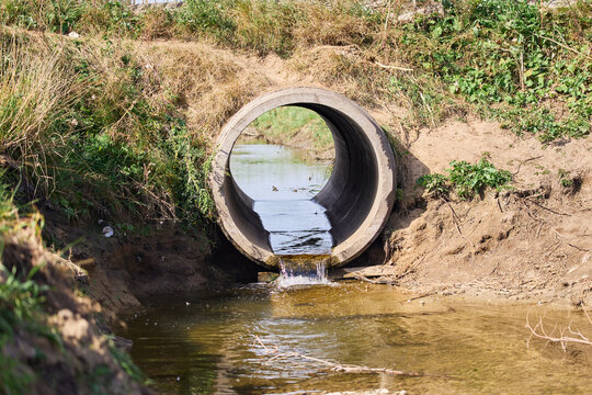 Concrete drainage culvert pipe discharging water into a stream in a rural landscape