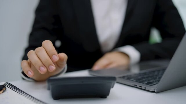Close-up of professional in formal suit using calculator and laptop for financial calculation and business analysis