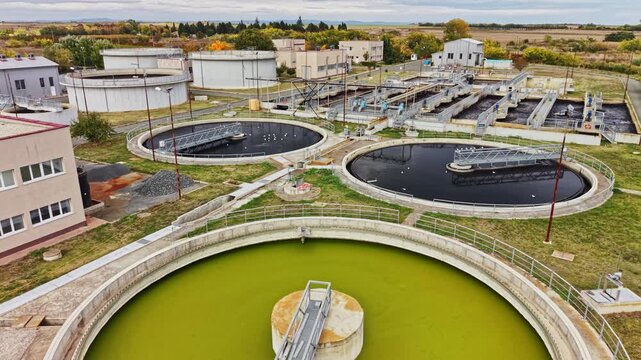 Circular treatment basins, pipes, buildings, and open channels fill a wastewater facility in a rural area during daylight.