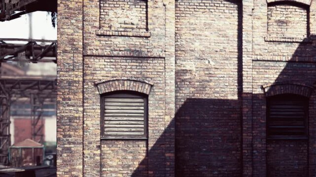 Sunlight shines on old brick buildings during day while dark shadows fall across the aged walls and closed windows
