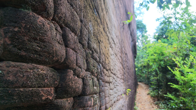 Ancient stone wall beside forest trail creates quiet travel scene with textured masonry, dense greenery, and peaceful outdoor atmosphere