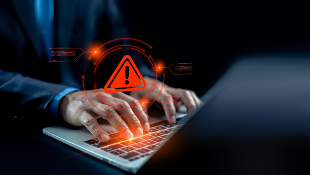 Business person typing on a laptop with a glowing red cyber threat warning sign and interface. Concept of cybersecurity risk, data breach, malware attack, and system vulnerability.