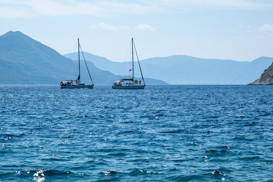 Two sailing yachts rest on deep blue Mediterranean waters with distant mountainous island coastlines stretching across the horizon near Aegina, Greece.