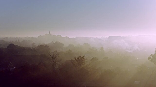 Aerial video across a shallow layer of ground fog and smoke drifting over a small farming community in serbian town of Temerin, Vojvodina. The sun sits low on the horizon at sunrise