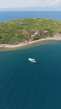 Aerial view of motorboat anchored near green coast of Cunda Island, Ayvalik. Vertical drone footage for summer travel and vacation. High quality 4k footage