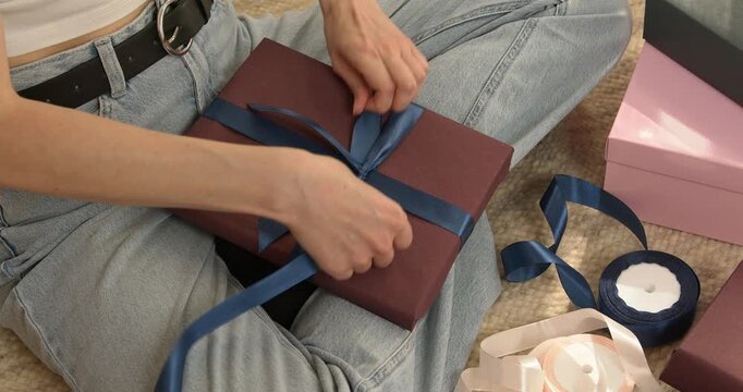 Woman hands tightening blue satin ribbon knot on gift box close up video.