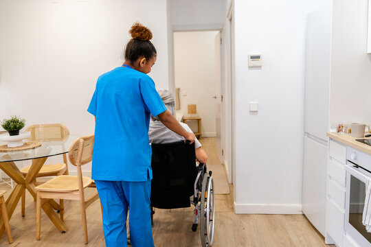 Home health nurse guiding an elderly woman in a wheelchair at home, providing mobility assistance and compassionate care
