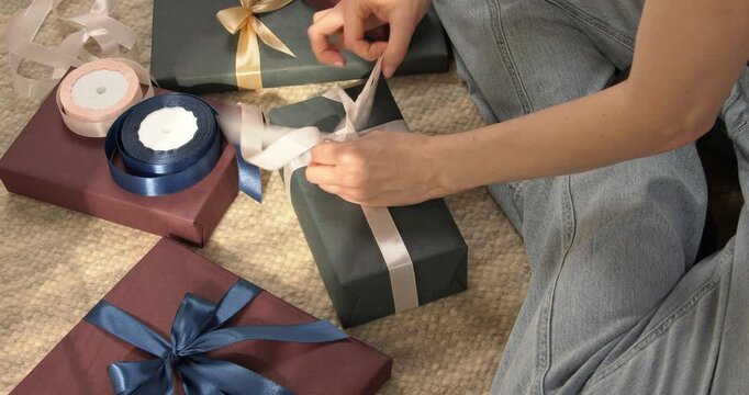 Woman hands tying white satin ribbon on green gift box with other presents around close up video.