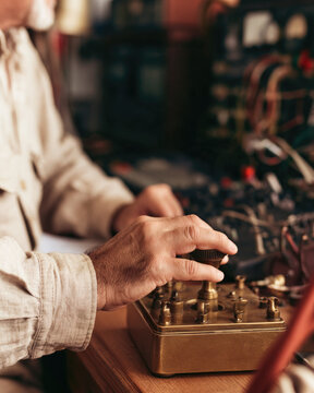 Vintage radio operator adjusting brass Morse key at wooden desk in sunlit workshop, creating tactile connection with analog communication heritage and focused craftsmanship