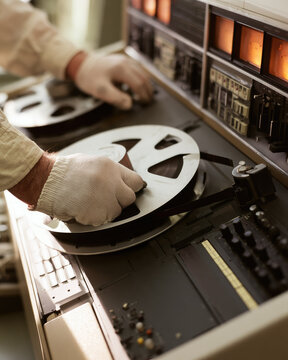 Hands mounting reel tape onto vintage magnetic tape recorder