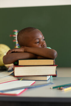 Schoolboy leaning on books at desk in a classroom