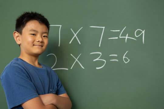 Schoolboy with arms crossed standing against greenboard in a classroom