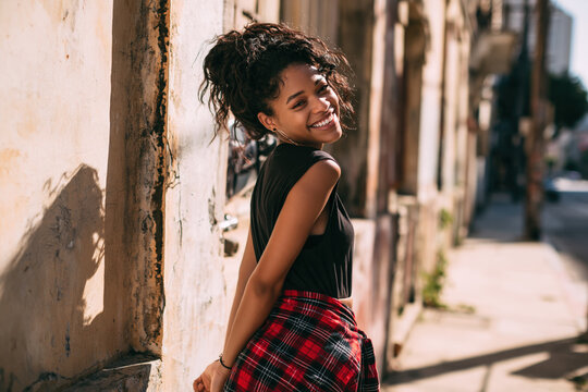 An African American girl in 90s-style grunge clothing stands on the street during the day.