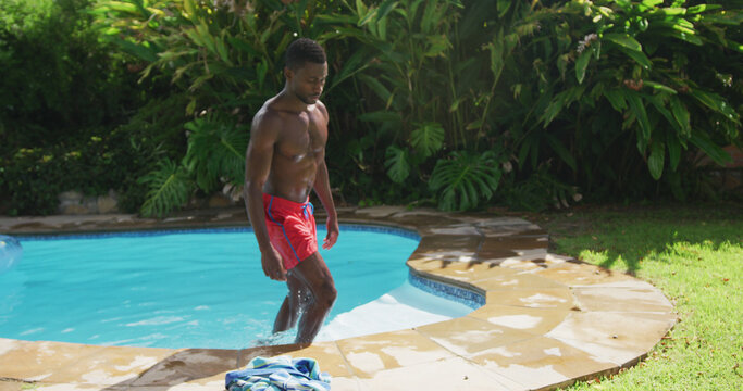 Handsome african american man walking out of in swimming pool in sunny garden
