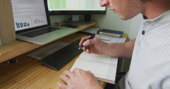 Focused caucasian man working remotely using computer, taking notes