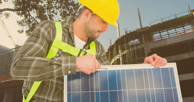Construction worker installing solar panel at building site, wearing safety gear